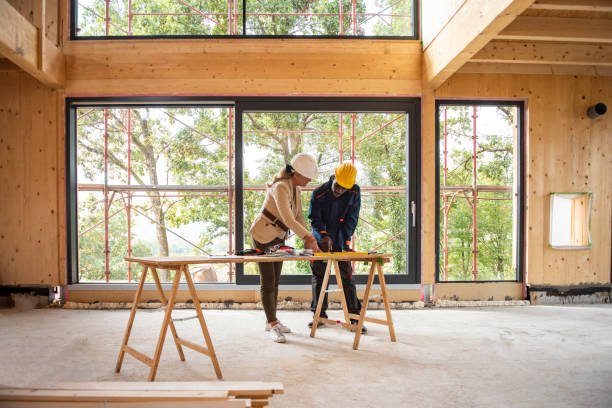 Two individuals collaborating on residential construction plans at a wooden table, surrounded by books and papers