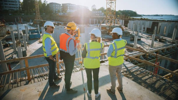 Three construction workers in hard hats stand on a commercial construction site, discussing project details.